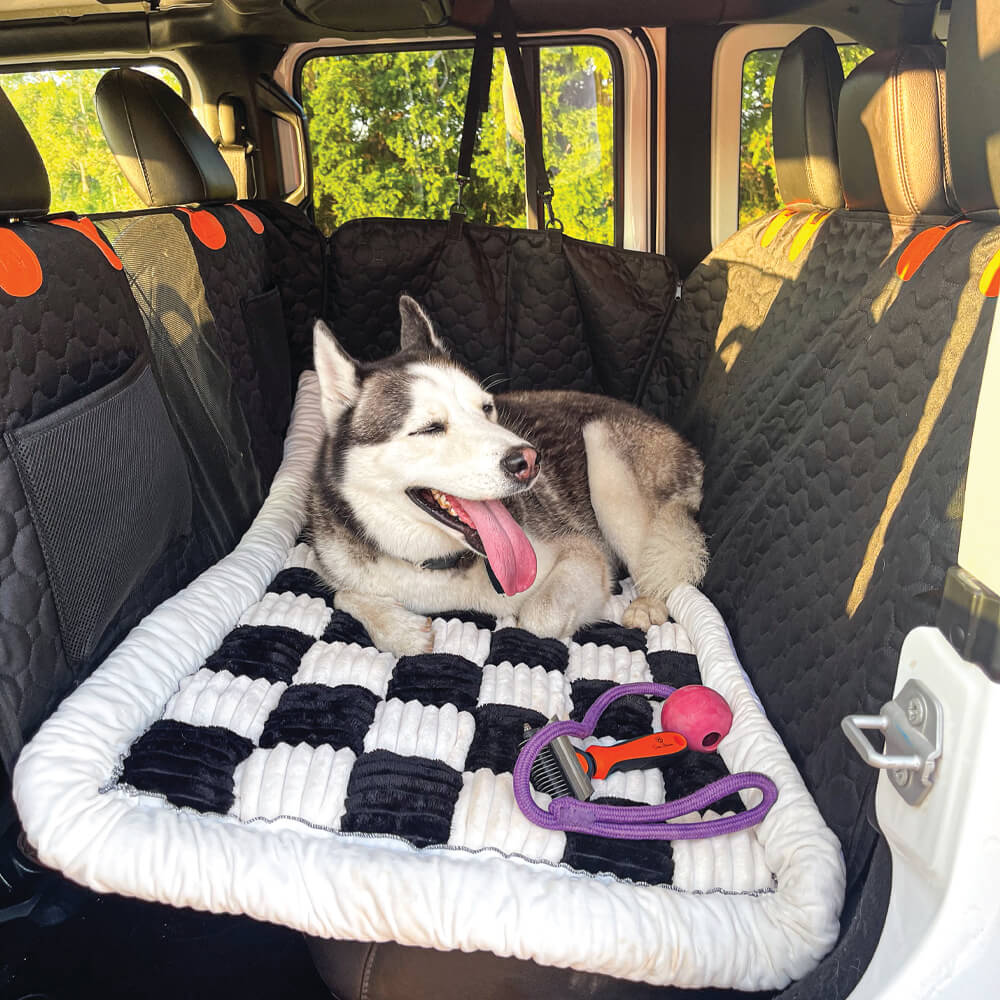 Husky relaxing on black plaid dog car bed with toys