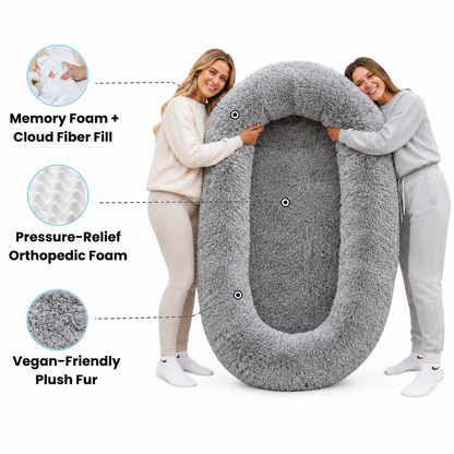 Two women holding a large, plush gray orthopedic pet bed with text callouts highlighting its features: 'Memory Foam + Cloud Fiber Fill,' 'Pressure-Relief Orthopedic Foam,' and 'Vegan-Friendly Plush Fur.'.